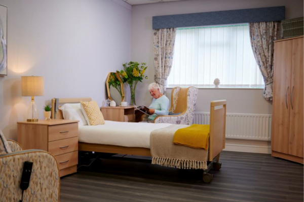 The Cadence bed, in a bedroom environment with a lady sat at a dressing table.